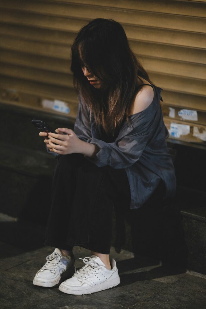 Woman experiencing functional freeze trauma response sitting alone on steps, looking at phone